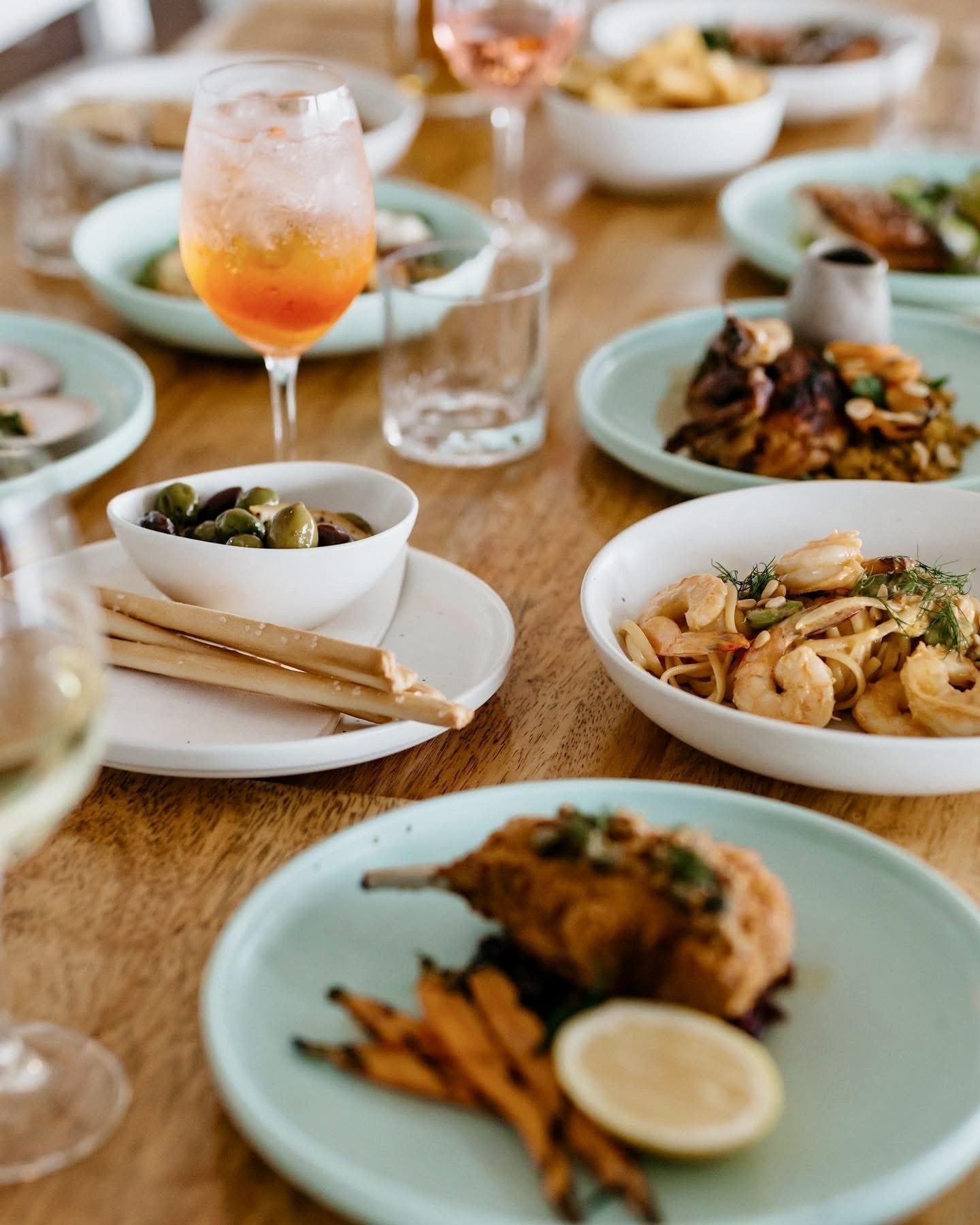 Dinner table spread with prawn pasta, chicken, olives and Aperol spritz