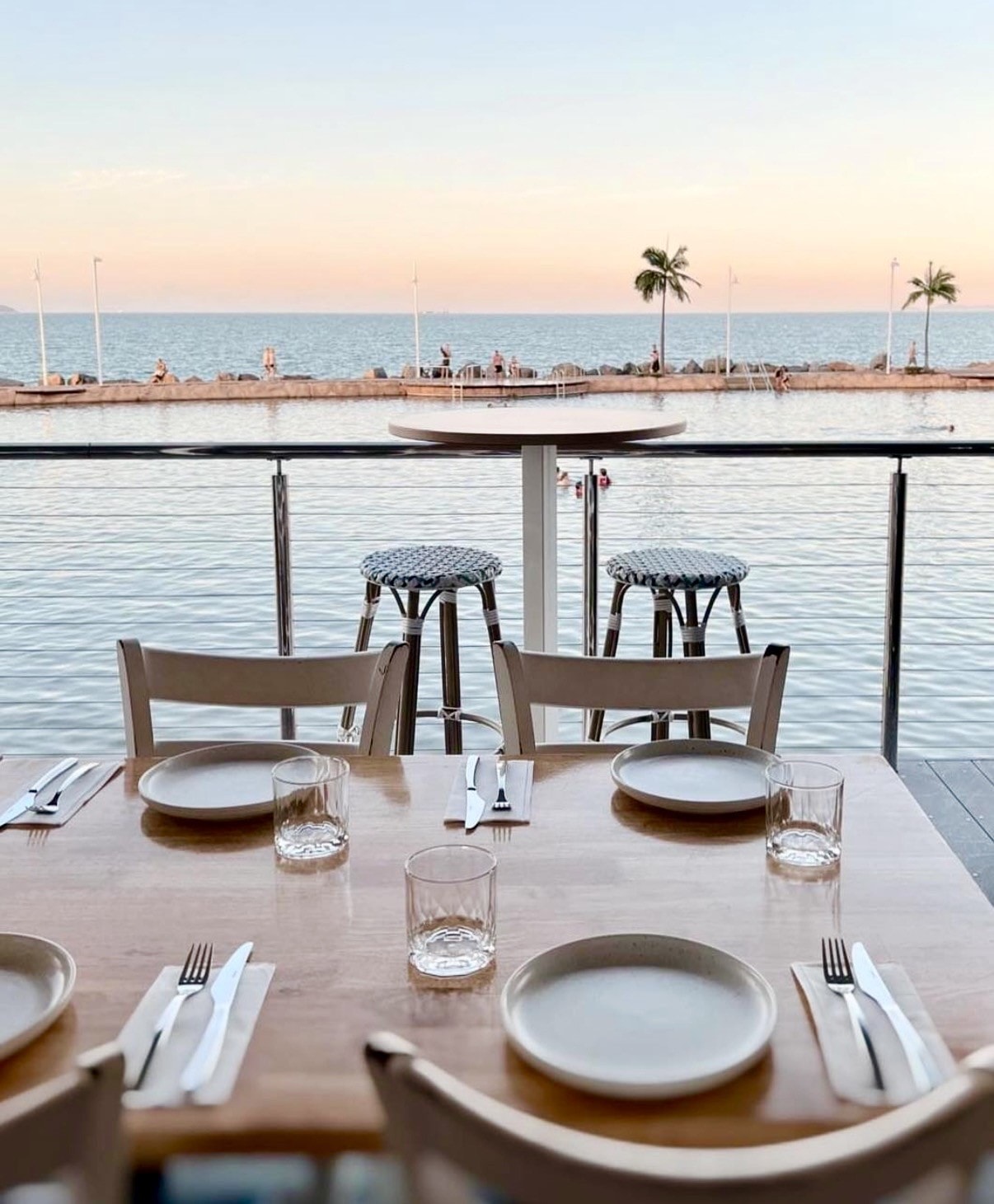 Dining table set for four with pool and ocean views at sunset